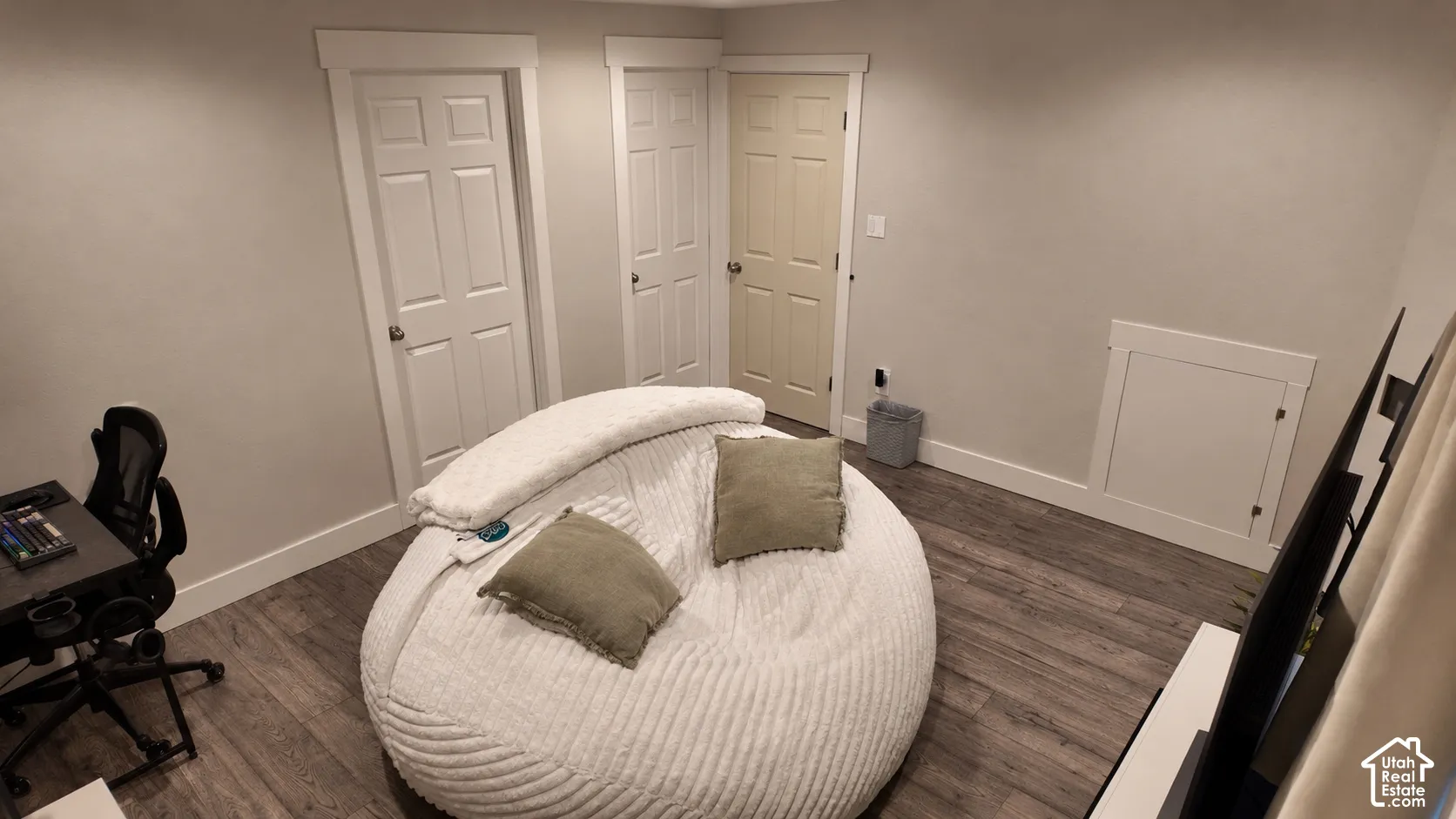 Room featuring wood-finish flooring, three interior doors with white trim, and a built-in wall access panel