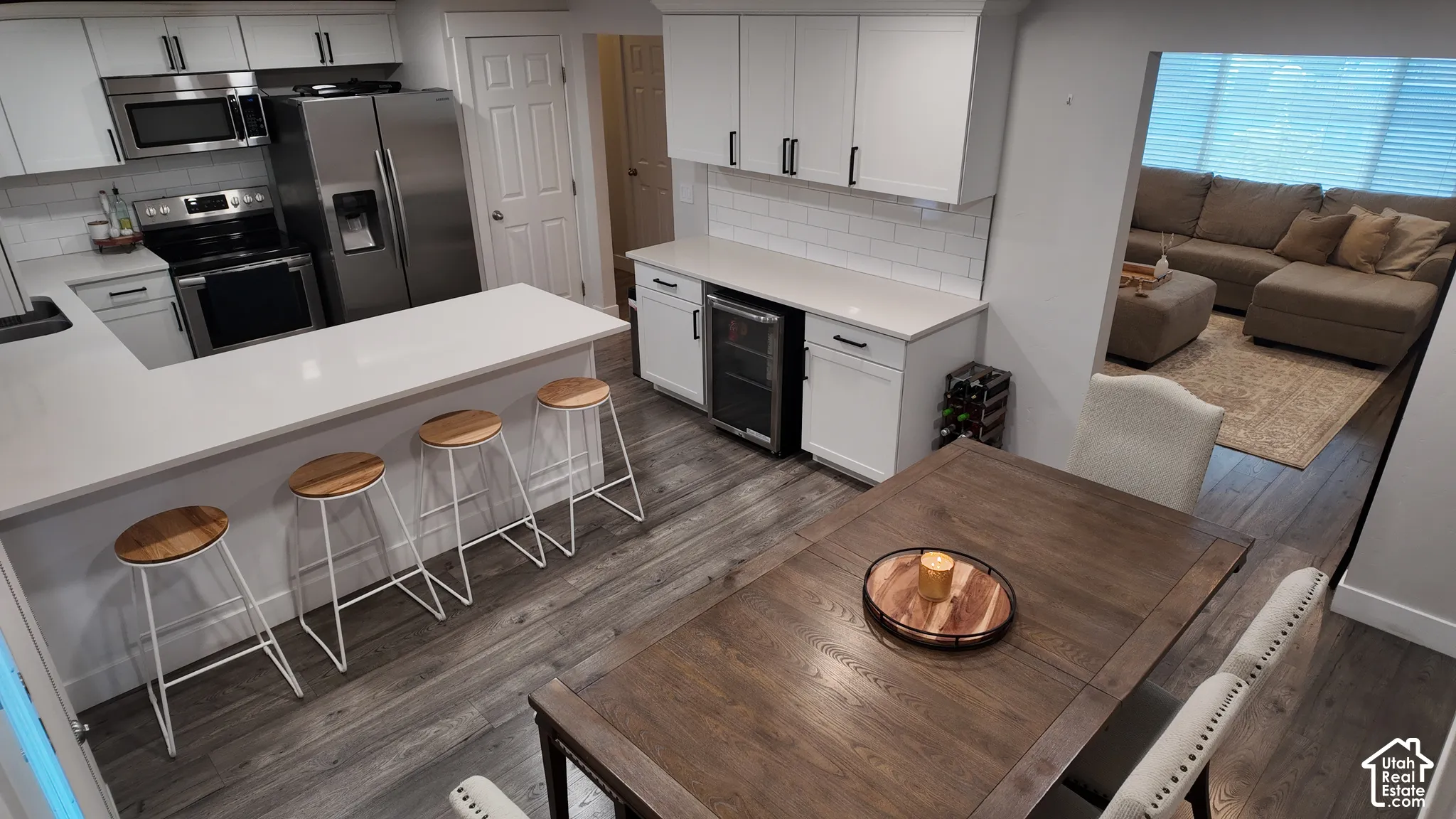 Kitchen featuring white cabinetry, solid-surface countertops, subway tile backsplash, stainless steel appliances, and integrated beverage cooler