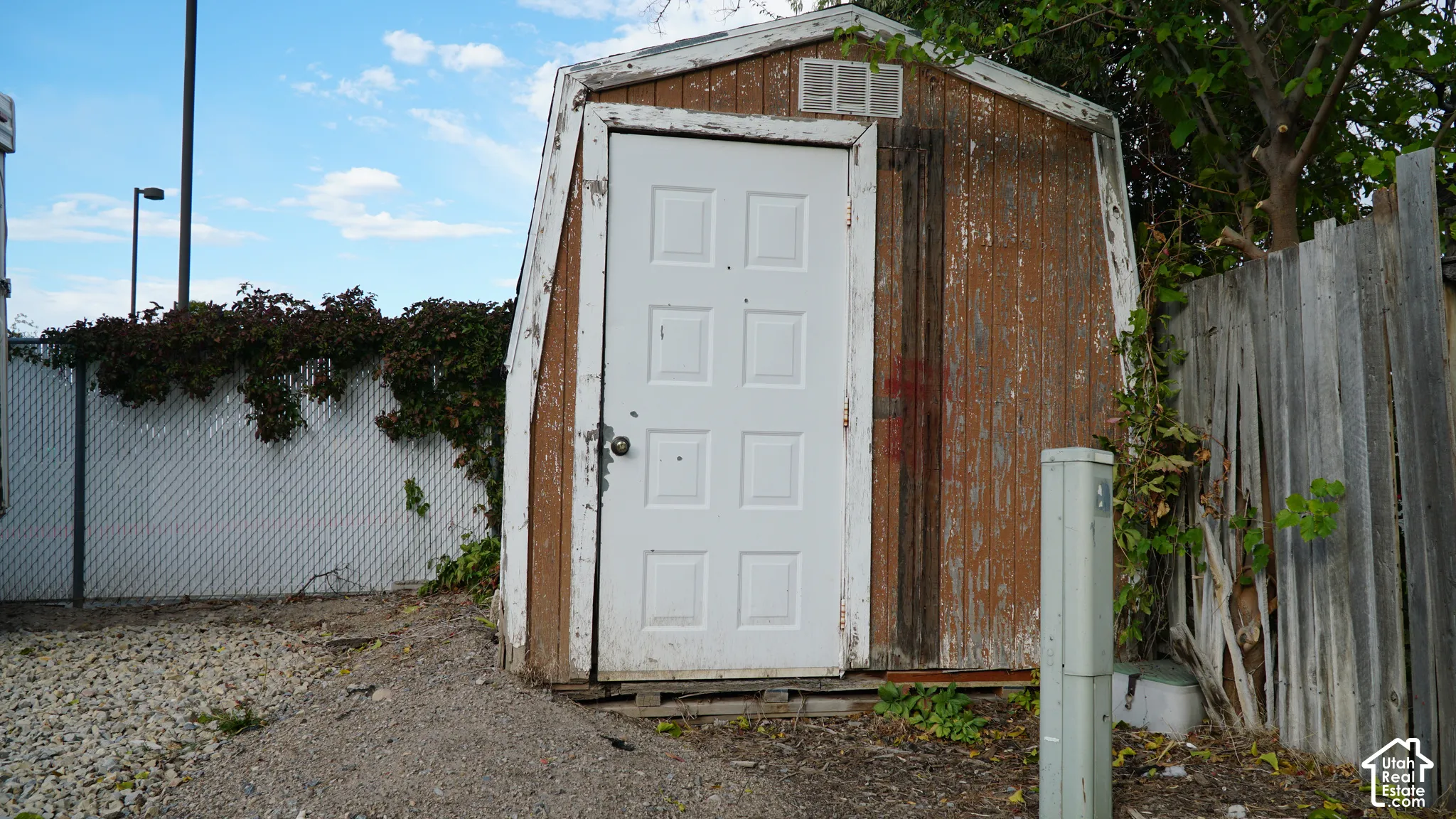 Detached wooden storage shed featuring a gambrel roof design, white paneled entry door, and exterior siding