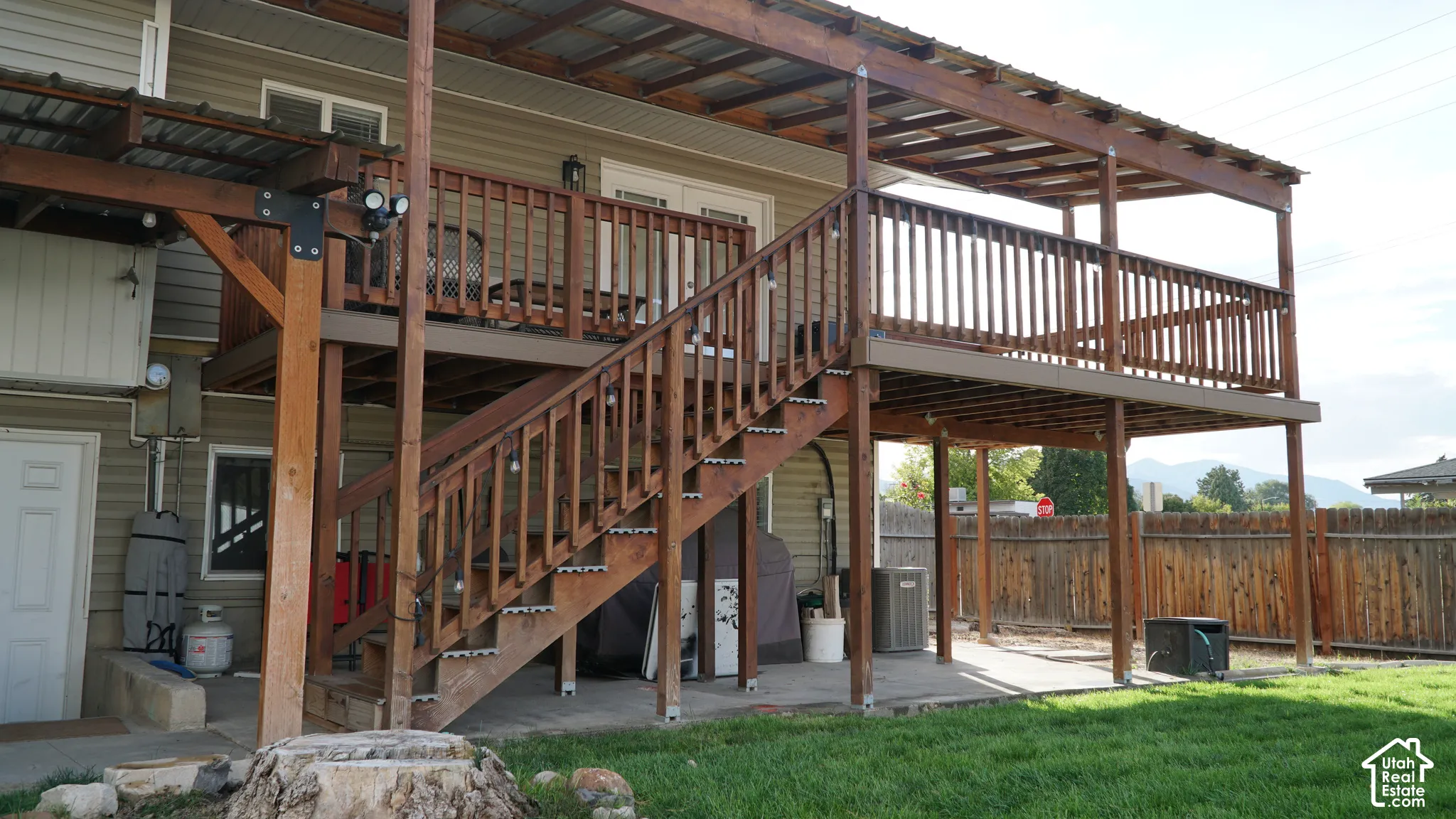 Elevated wooden deck featuring a metal-panel roof covering, wooden railings, and a matching staircase descending to a concrete patio