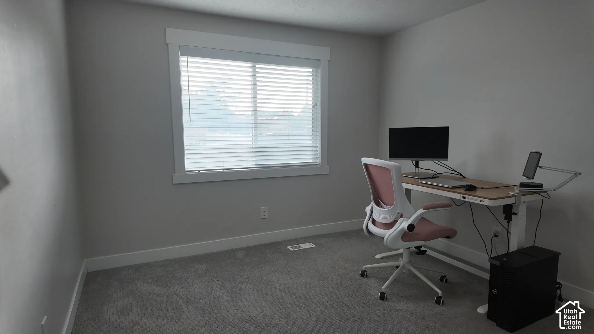 Neutral-toned walls, plush wall-to-wall carpeting, and a wide window featuring crisp white casing and horizontal blinds