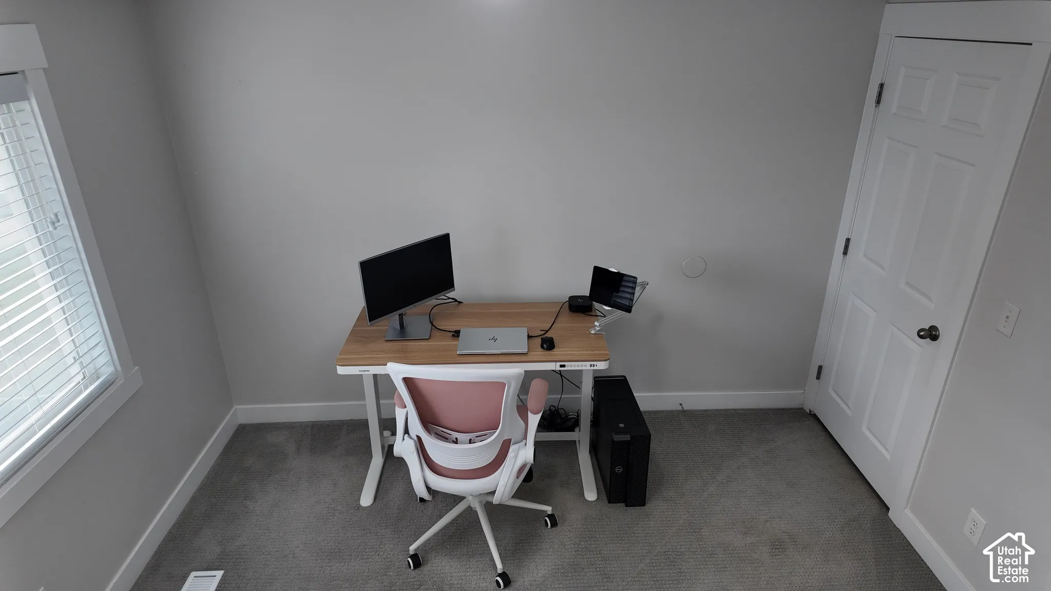 Room featuring neutral-toned walls, gray carpeting, a window with horizontal blinds, and a single-panel interior door with brushed metal hardware