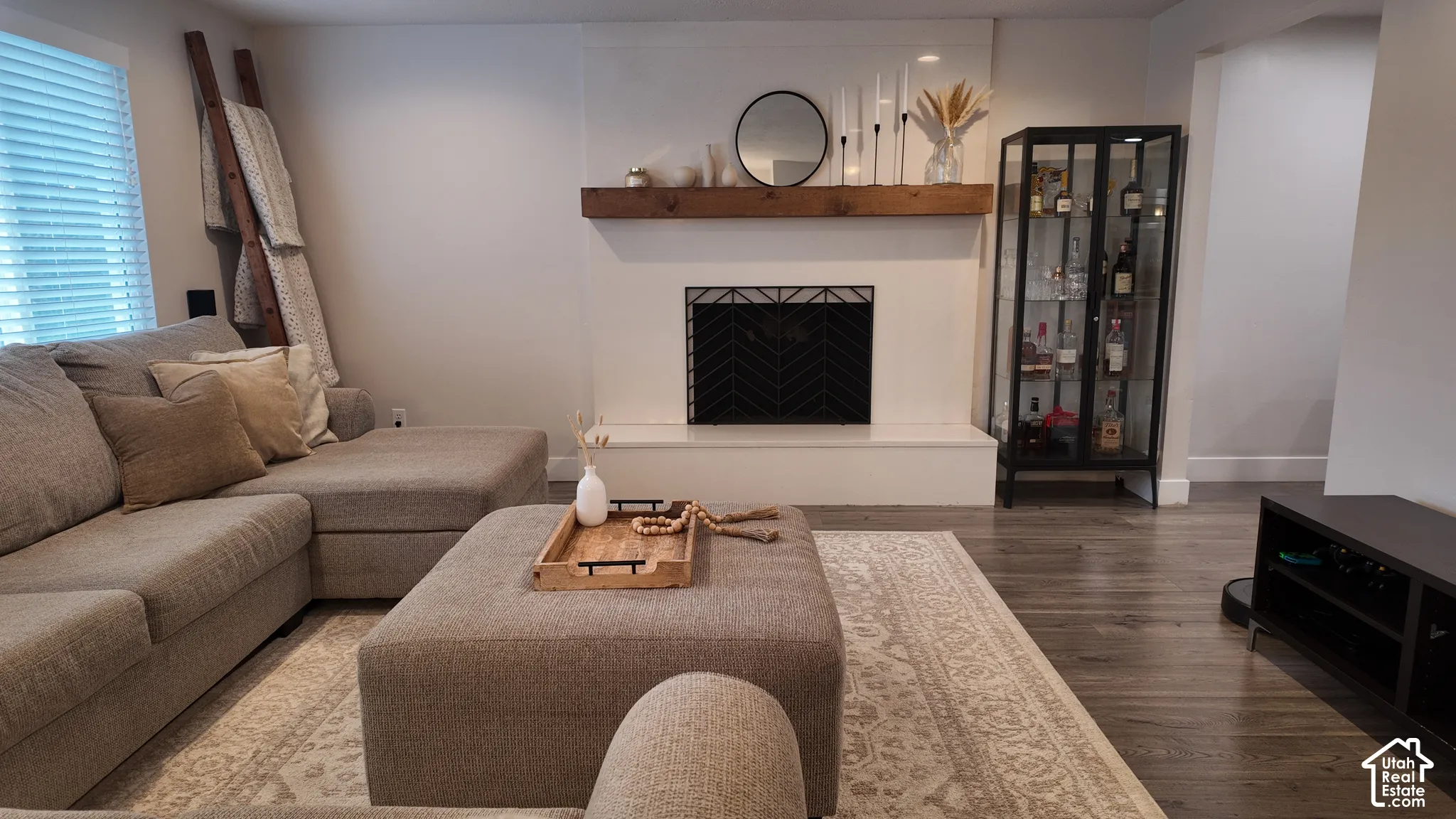 Fireplace featuring a custom-built hearth, clean-lined white surround, wood-finish mantel, and patterned metal fire screen, complemented by wood-finish flooring