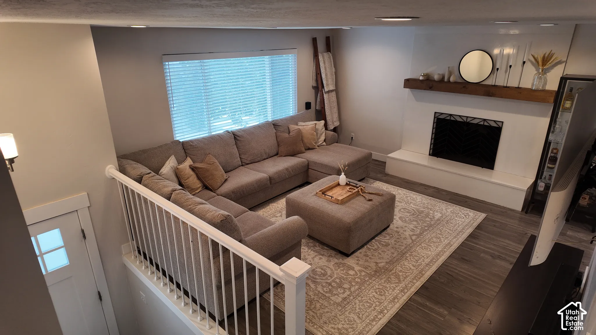 Living area featuring a fireplace with a smooth white hearth and a wood mantel, wood-finish flooring, recessed lighting, and a white balustrade railing