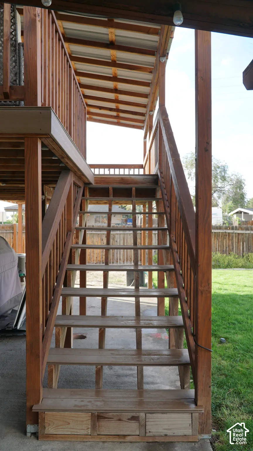 Covered wooden staircase featuring an elevated deck with wood-finish railings and a concrete patio foundation