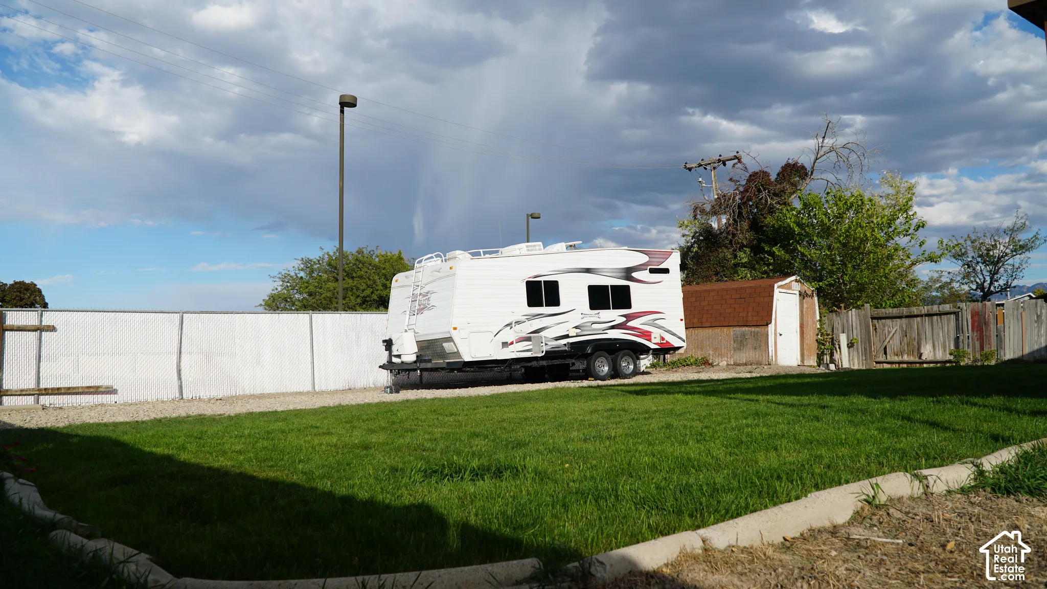 Expansive backyard featuring a manicured lawn, gravel parking area, stone-border edging, and a detached storage shed