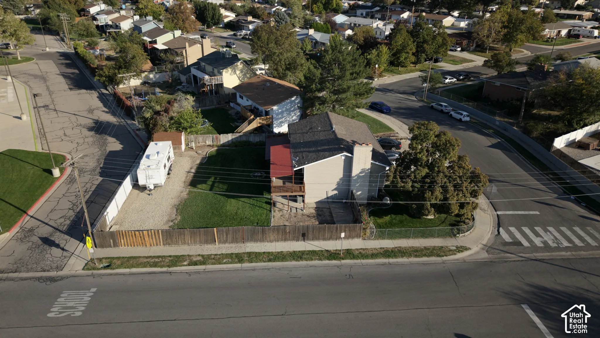 Aerial perspective of a corner lot featuring a fenced-in yard, paved off-street parking area, wood-style exterior siding, and a gabled roof