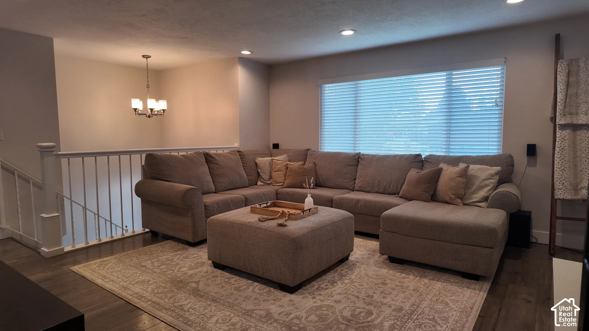 Open-concept living space featuring wood-finish flooring, recessed lighting, a multi-arm chandelier, and a white baluster staircase railing