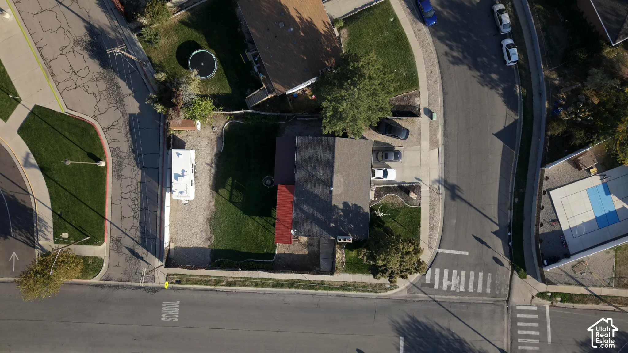 Aerial perspective of a corner lot featuring a private driveway, gravel side parking area, fenced lawn, and a multi-section roofline