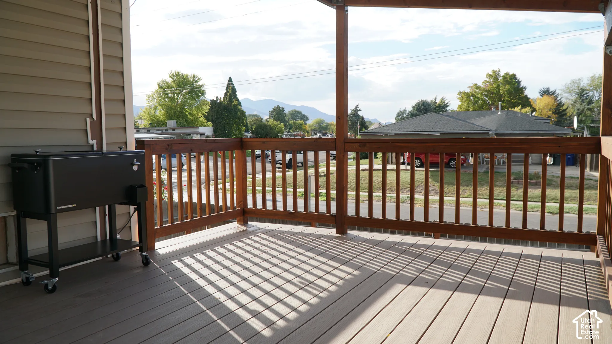 Covered wood deck featuring stained wooden railings, composite decking material, and mountain backdrop