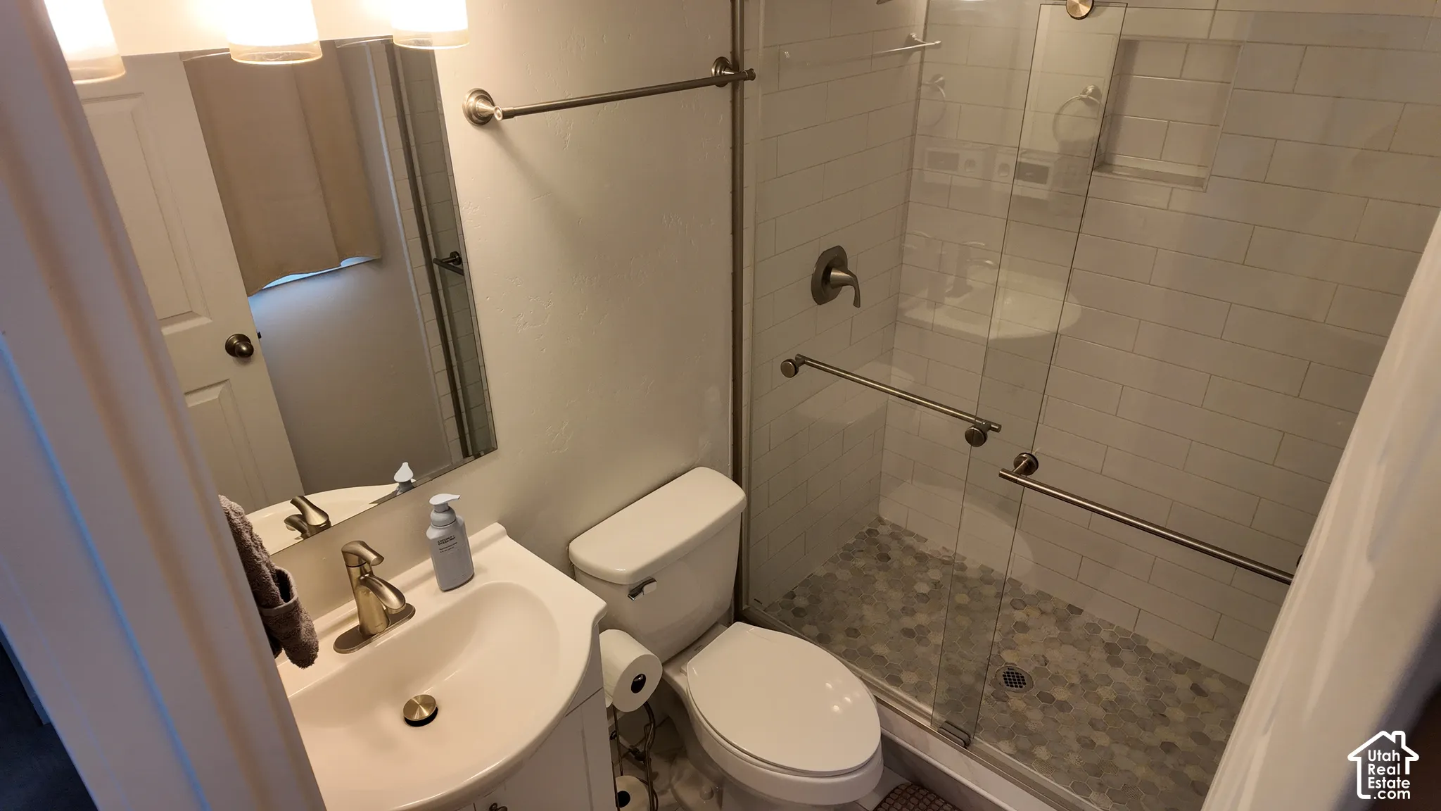 Bathroom featuring a vanity with an integrated sink, brushed metal faucet, shower with white subway tile surround, built-in wall niche, and pebble-style floor tiling