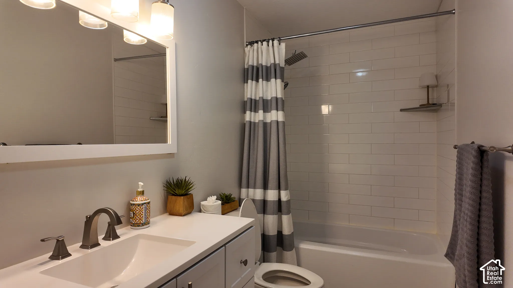 Bathroom featuring a white vanity with a rectangular basin, metallic finish faucet, framed mirror, and a shower-tub combination with white subway tile surround