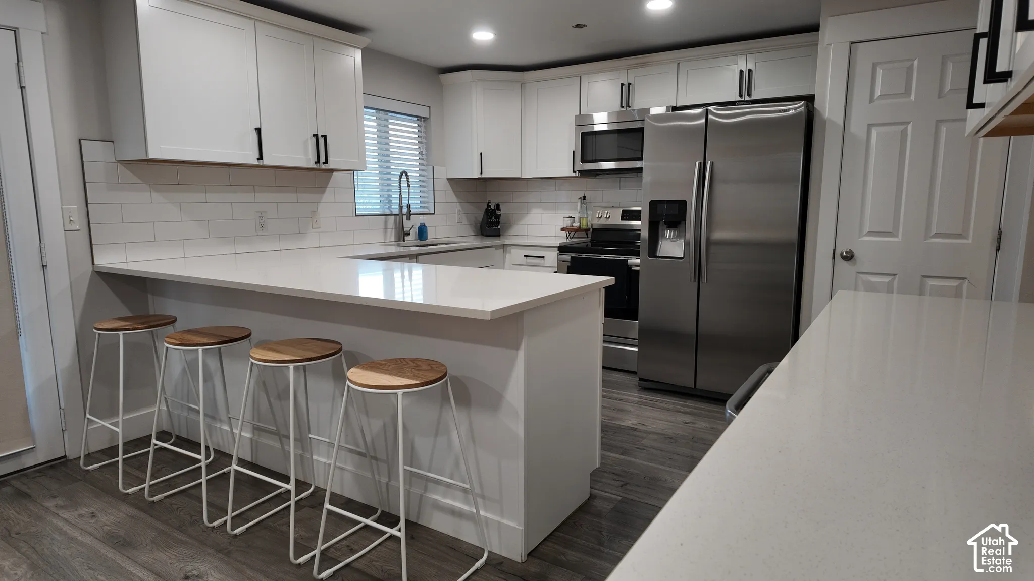 Kitchen featuring white cabinetry, quartz countertops, subway tile backsplash, stainless steel appliances, and wood-finish flooring