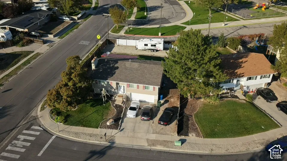Aerial perspective of a multi-level residence featuring an attached two-car garage, concrete driveway, front yard landscaping, and fenced perimeter