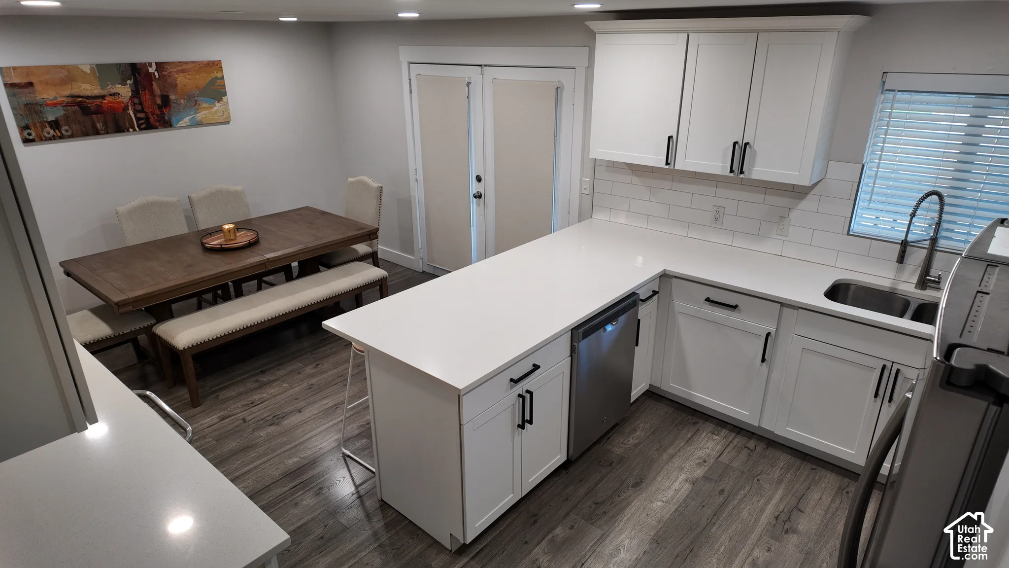 Kitchen featuring white shaker-style cabinetry, solid-surface countertops, subway tile backsplash, stainless steel dishwasher, and wood-finish flooring