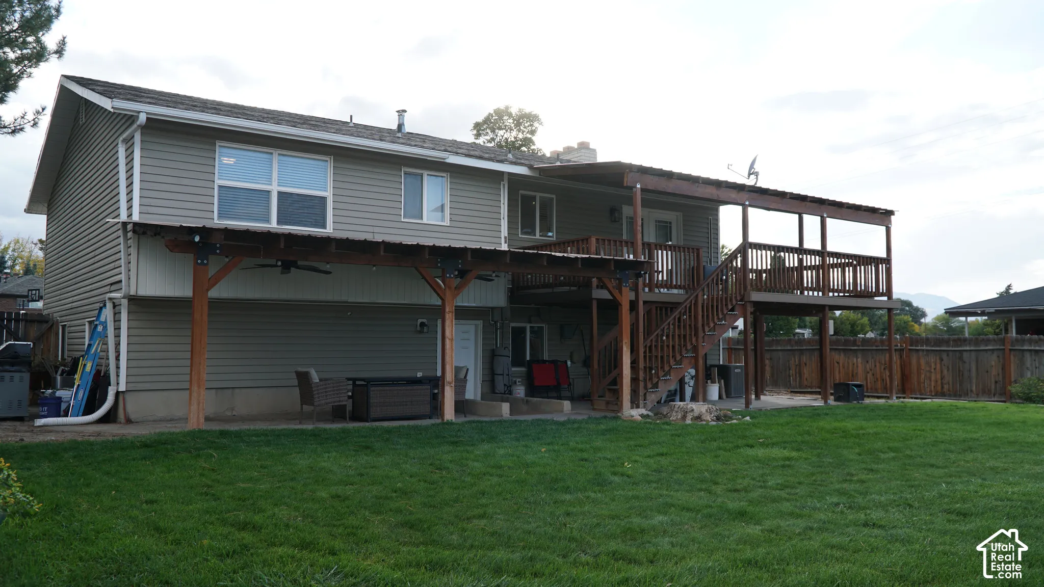 Exterior rear elevation featuring horizontal siding, a multi-level wood deck, a covered patio with timber support beams, and a fenced backyard