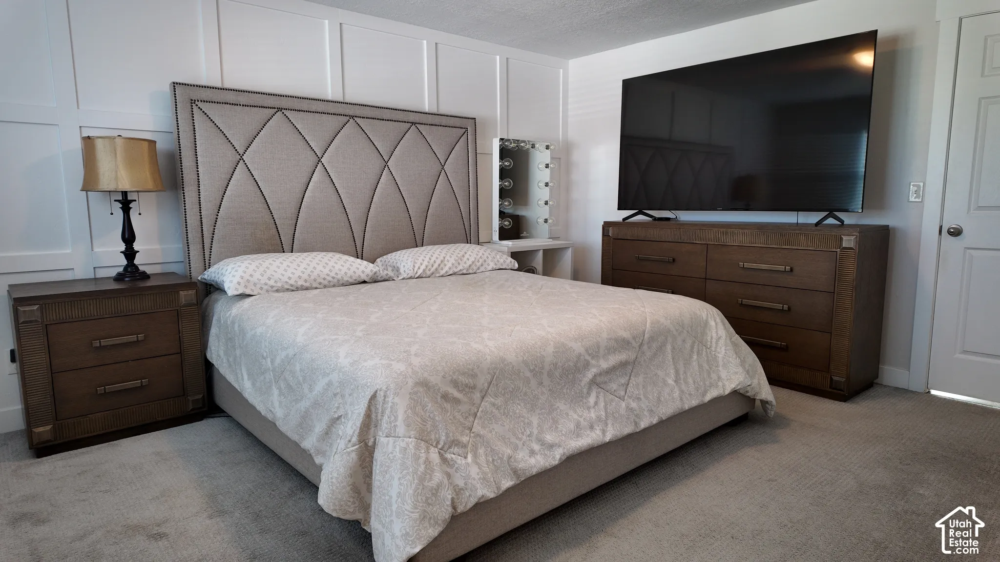 Bedroom featuring white wainscoting wall paneling, wall-to-wall carpeting, and a four-panel interior door