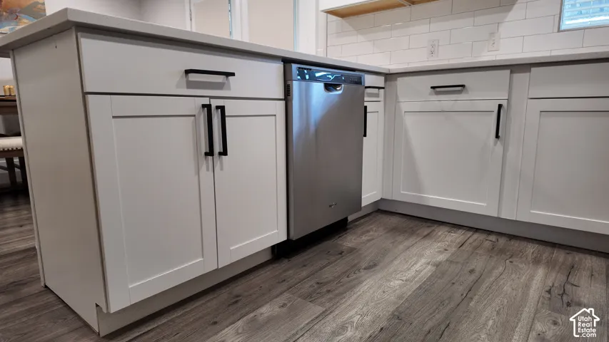 Kitchen island featuring white shaker-style cabinetry, matte black hardware, stone-finish countertops, stainless steel dishwasher, and subway tile backsplash over wood-finish flooring