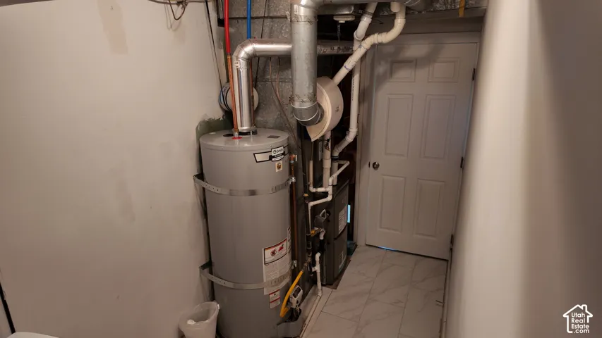 Mechanical utility space featuring a cylindrical water heater, forced-air furnace, exposed metal ductwork, and white tile flooring