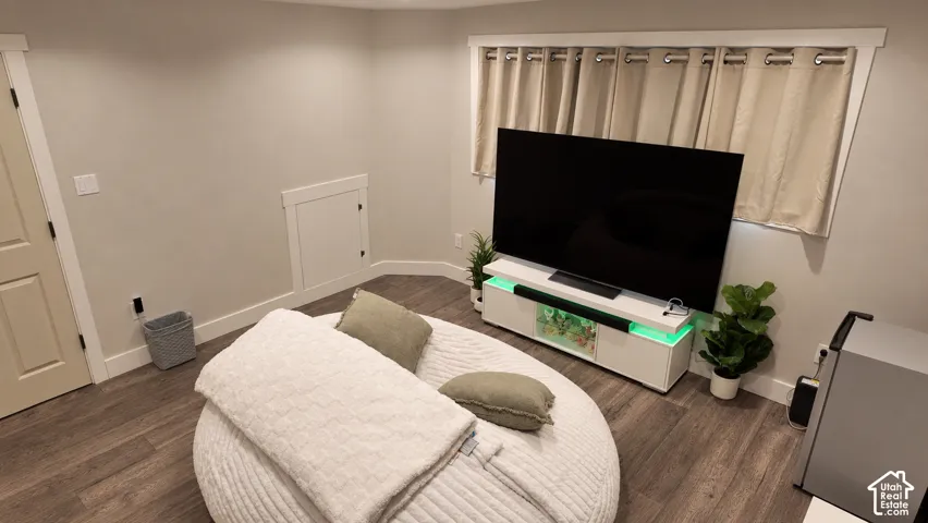 Interior space featuring wood-finish flooring, neutral wall tones, window treatments with grommet headers, and a built-in access panel