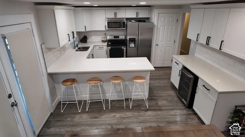 Kitchen featuring white shaker cabinetry, stone-finish countertops, subway tile backsplash, stainless steel appliances, and wood-finish flooring