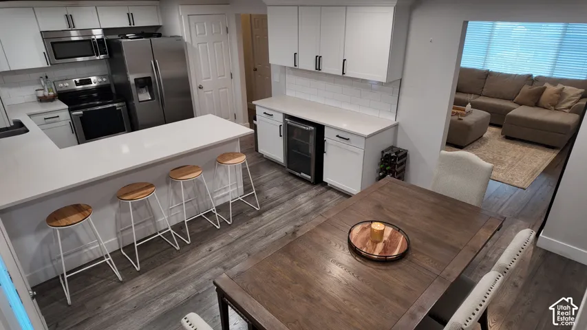 Kitchen featuring white cabinetry, solid-surface countertops, subway tile backsplash, stainless steel appliances, and integrated beverage cooler