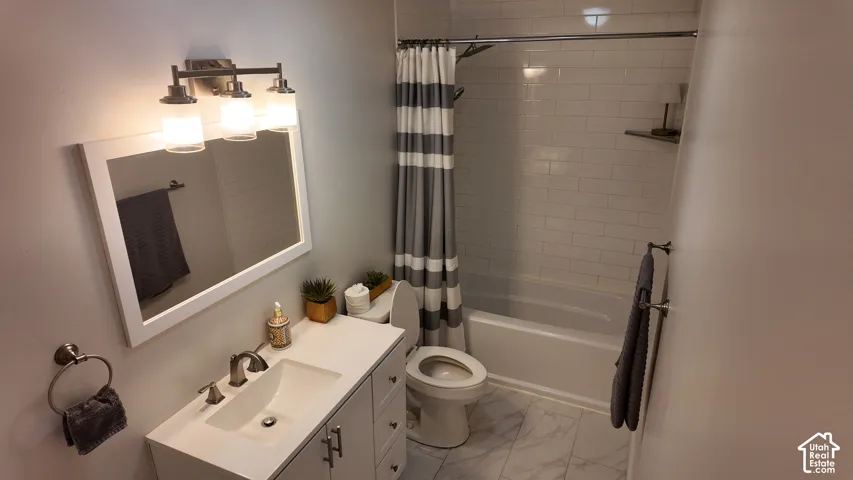 Bathroom featuring a vanity with a white countertop and integrated sink, a rectangular framed mirror with three-light fixture, tub-shower combination with white subway tile surround, and stone-finish flooring