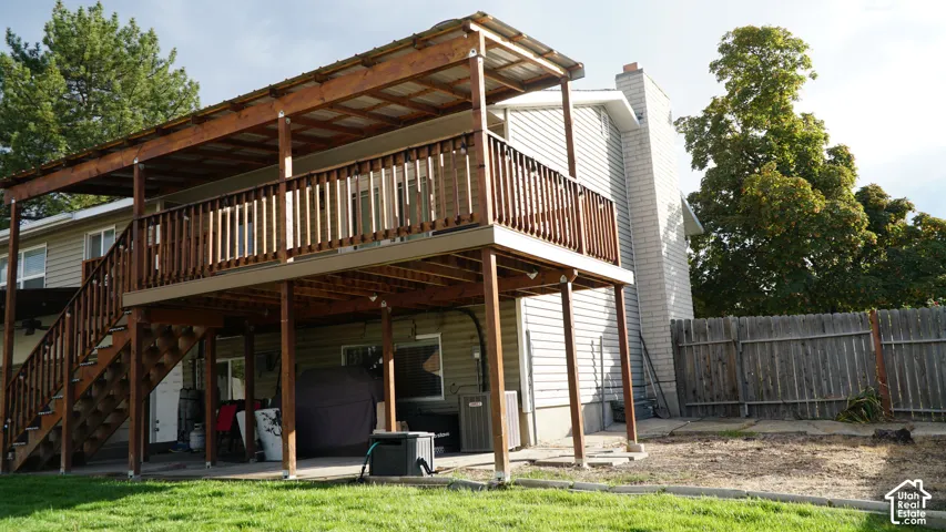 Two-story elevated wood deck with a covered upper level, integrated staircase, exterior brick chimney, and privacy fencing