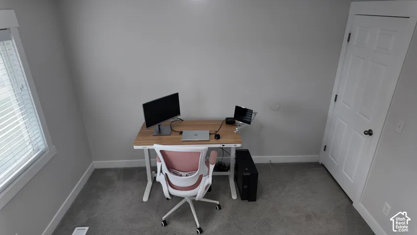 Room featuring neutral-toned walls, gray carpeting, a window with horizontal blinds, and a single-panel interior door with brushed metal hardware