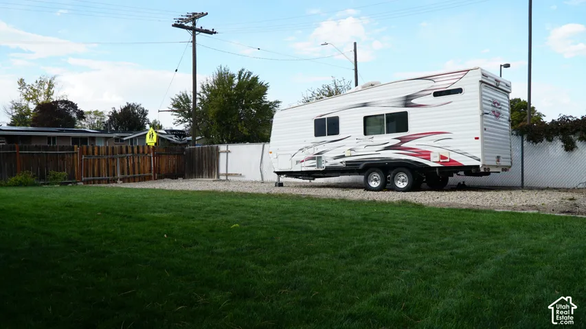 Backyard featuring a manicured lawn, a gravel parking area, and perimeter wood and chain-link fencing