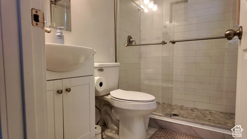 Bathroom featuring a white pedestal-style vanity with cabinet storage, glass-enclosed shower with white subway tile surround, pebble-style shower floor, and metal hardware