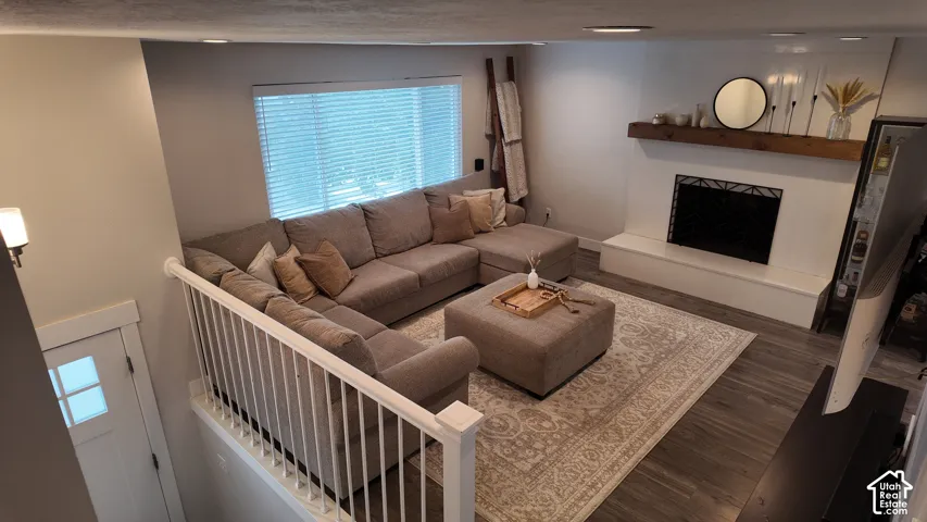 Living area featuring a fireplace with a smooth white hearth and a wood mantel, wood-finish flooring, recessed lighting, and a white balustrade railing