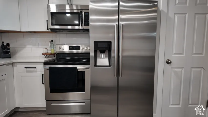 Stainless steel appliances, white cabinetry with matte black hardware, white subway tile backsplash, and quartz countertops
