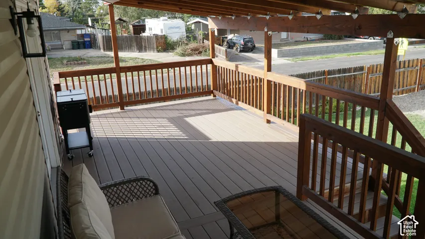 Covered composite deck featuring wood-finish railings, an overhead timber beam structure, and integrated wall-mounted exterior lighting
