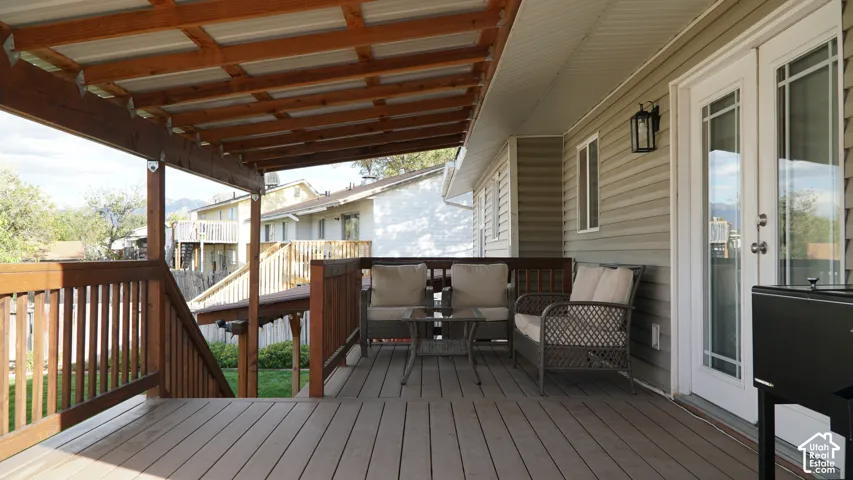 Covered wood deck featuring a timber-frame pergola, horizontal siding, and double glass-paned doors with integrated wall-mounted exterior lighting