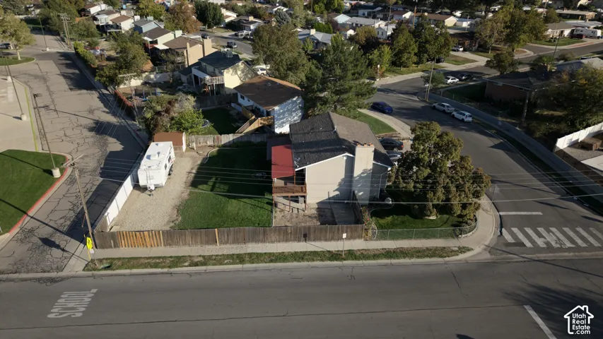 Aerial perspective of a corner lot featuring a fenced-in yard, paved off-street parking area, wood-style exterior siding, and a gabled roof