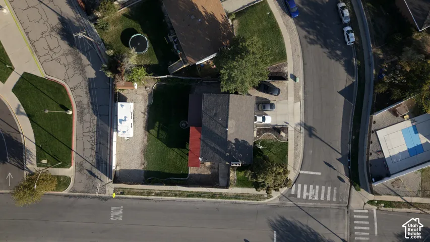 Aerial perspective of a corner lot featuring a private driveway, gravel side parking area, fenced lawn, and a multi-section roofline