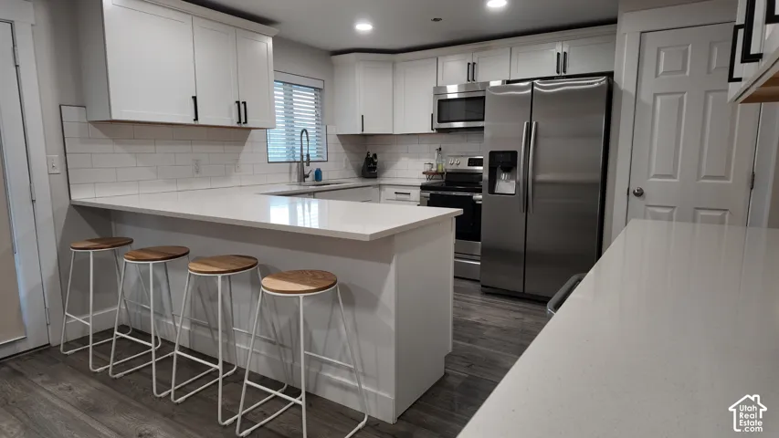 Kitchen featuring white cabinetry, quartz countertops, subway tile backsplash, stainless steel appliances, and wood-finish flooring