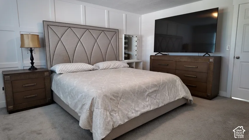 Bedroom featuring white wainscoting wall paneling, wall-to-wall carpeting, and a four-panel interior door