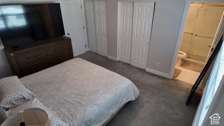 Wall-to-wall carpeting, dual bifold closet doors, and attached bathroom featuring a walk-in shower with a glass enclosure