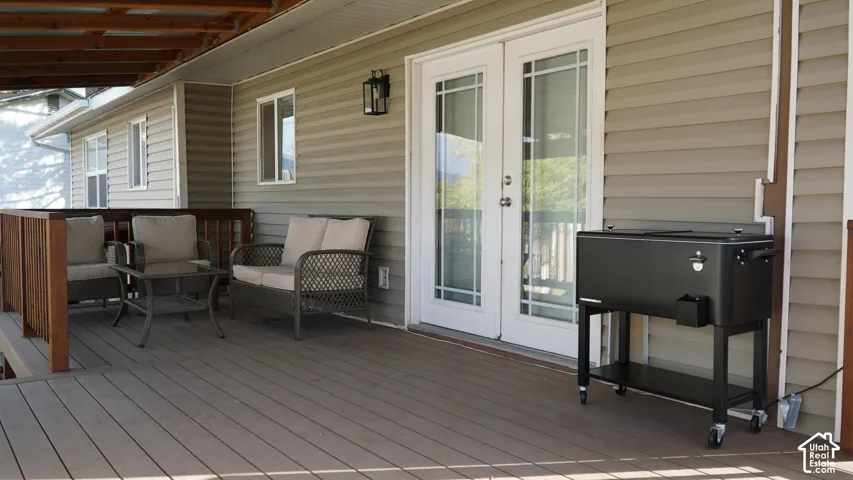 Covered wood-plank deck featuring horizontal vinyl siding, dual-pane French doors, and a decorative wall-mounted lantern light fixture