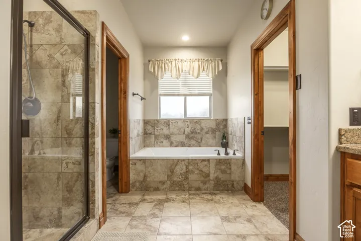 Bathroom featuring a tiled shower enclosure with a glass door, a built-in soaking tub with tile surround, wood-trimmed door frames, and neutral tile flooring
