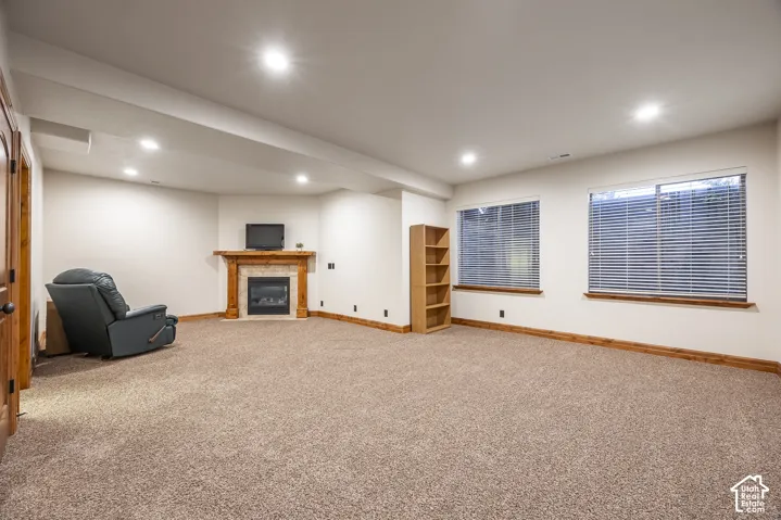 Neutral interior featuring recessed lighting, carpeting, dual windows with blinds, and a built-in stone-surround fireplace with a wooden mantel
