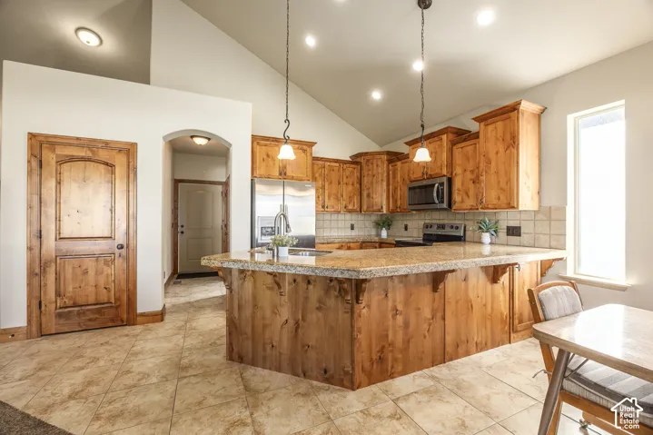 Kitchen featuring vaulted ceilings, stained wood cabinetry, stone-style tile flooring, stone-surfaced countertops, and pendant lighting
