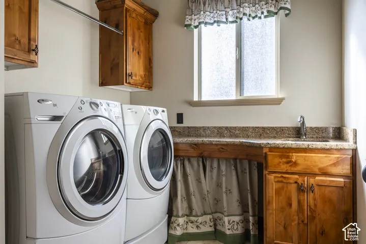 Laundry space featuring wood-finish wall cabinetry, stone-surface countertop with an integrated basin, faucet fixture, and window