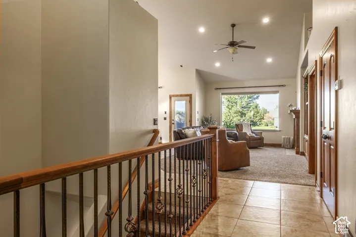 Staircase featuring a wood handrail with metal balusters, large-format tile flooring, recessed ceiling lighting, a ceiling fan, and vaulted ceilings