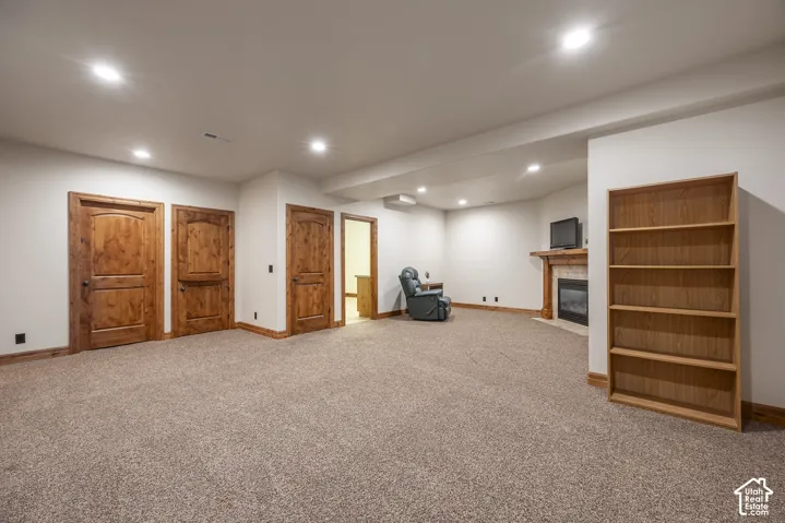 Spacious interior featuring recessed lighting, carpeted flooring, three solid wood doors, a built-in wooden bookshelf, and a fireplace with a mantel