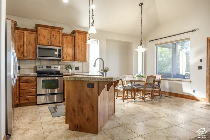 Kitchen featuring wood cabinetry, a center island with a stone-finish countertop, stainless steel appliances, ceramic tile flooring, and vaulted ceilings