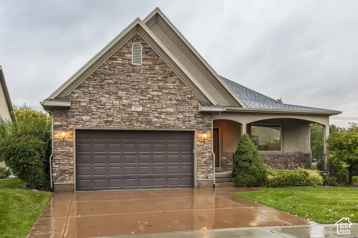 Exterior facade featuring stone veneer, stucco siding, a covered entryway, a concrete driveway, and a two-car garage