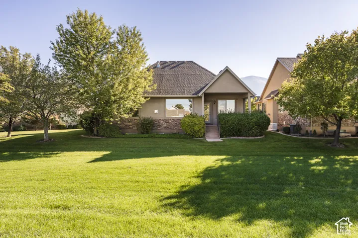 Single-story residence featuring a stone-veneer foundation, shingle roof, covered entryway, and an expansive lawn with mature trees